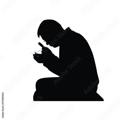 Silhouette of a person with glasses inspecting a small object with a magnifying glass closely