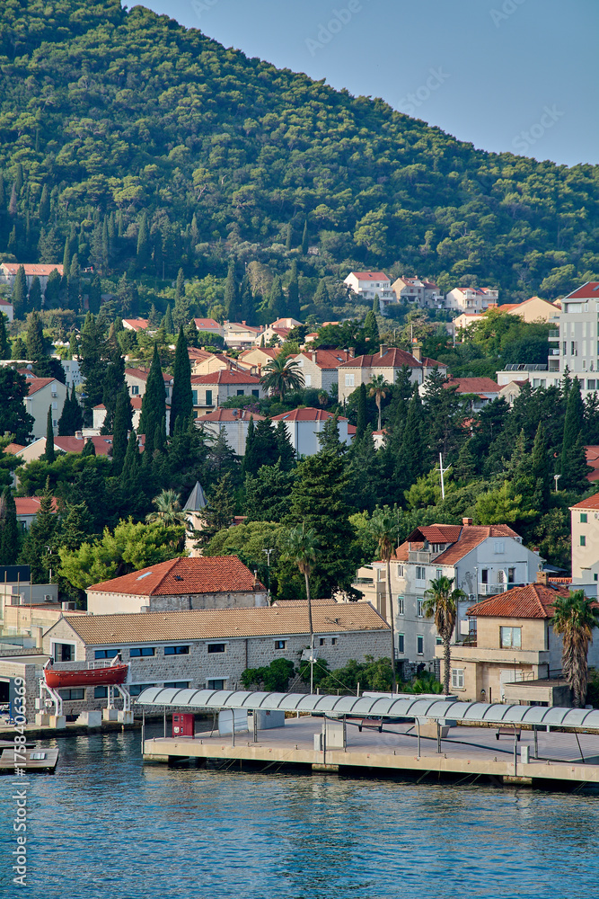 Obraz premium A lone motorboat navigates the calm blue waters of the Adriatic Sea, with the picturesque coastline of Dubrovnik and its hills in the background.