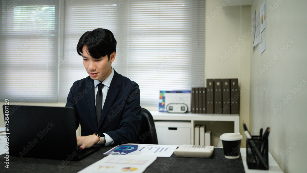 Fototapeta premium Asian business man in suit using laptop and tablet while sitting at her working place. Concentrated at work.