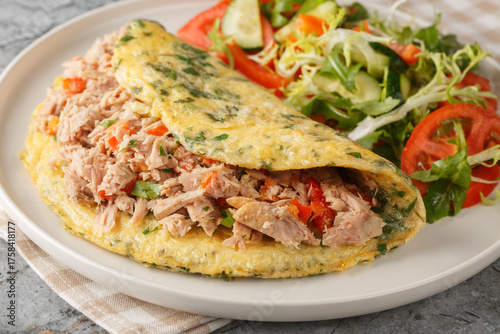 Omelette stuffed with canned tuna and peppers and served with vegetable salad close-up in a plate on the table. Horizontal