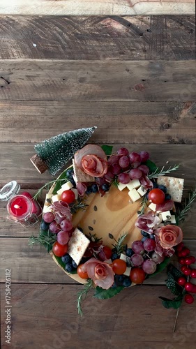 Charcuterie board with cheese, grapes, cranberries, tomatoes, ham and with Christmas decorations around it.