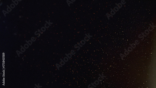 Dark abstract background with scattered dust particles, cinematic film grain texture, and subtle warm light. Perfect for retro photography effects, video overlays, and grungy design projects.