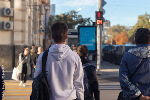 A young man waiting for the traffic light to turn green to cross the road.
