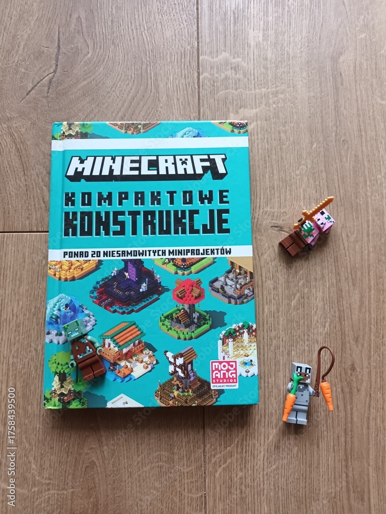 Fototapeta premium Polish edition of the 'Minecraft Kompaktowe Konstrukcje' guide book for compact builds, featuring two Minecraft-themed toy figures on a wooden floor