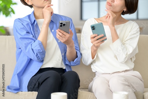 Принти на полотні A woman sitting on the sofa and looking at her smartphone is worried