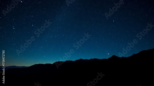 A breathtaking view of the starry night sky illuminates the dark silhouette of a mountain range against the twilight horizon, offe a sense of cosmic wonder.