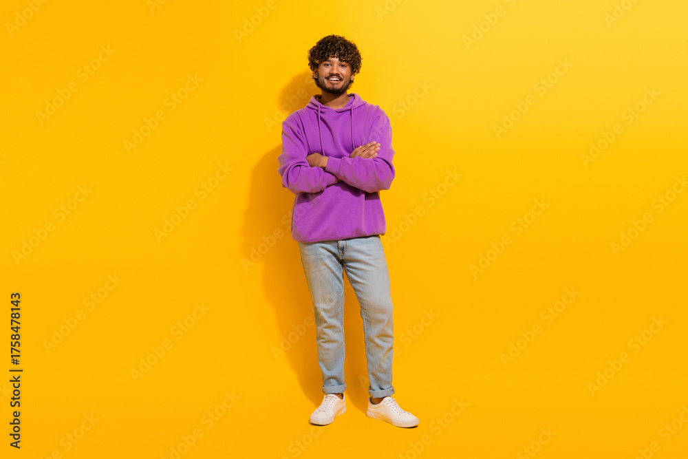 Fototapeta premium Young man in purple hoodie smiling confidently on a vibrant yellow background, embodying modern casual fashion and youthful energy