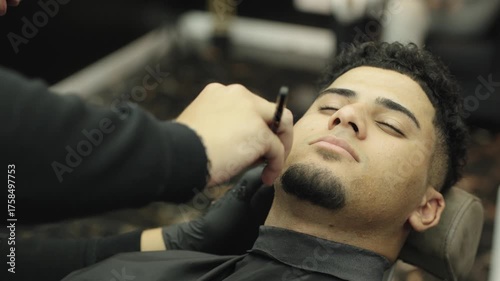 Barber shaping a client's goatee with a straight razor in a barbershop