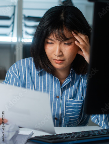 Serious Young Asian Businesswoman reading financial report document, reviewing data and information for making decision, planning business strategy feeling thought and stress in corporate office night