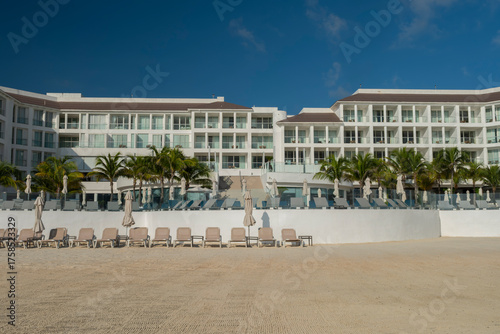 Tourist resort hotel and lounge chairs by the ocean at white sand clean beach, Playa del Carmen, Mexico. Blue sky, sunny early morning. Vacation, tourism, south destination travel concept.