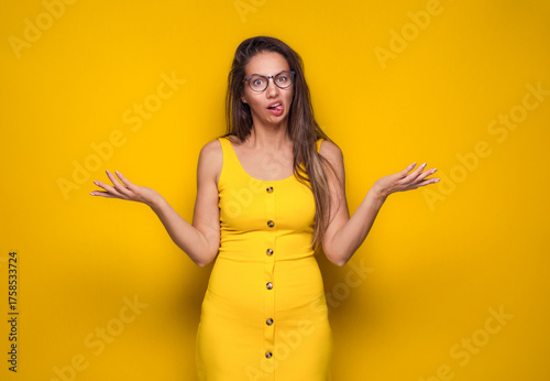 Confused young woman shrugging shoulders, don't know what to say, isolated on yellow background. Body language.