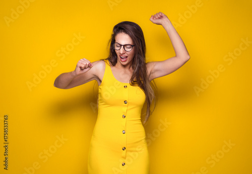 Excited young woman with clenched fist or hands celebrate success, isolated on yellow background.