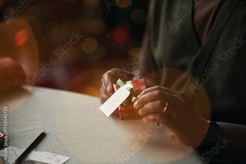 Fényképezés Middle aged Black man wrapping small Christmas gift box, attaching gift tag with