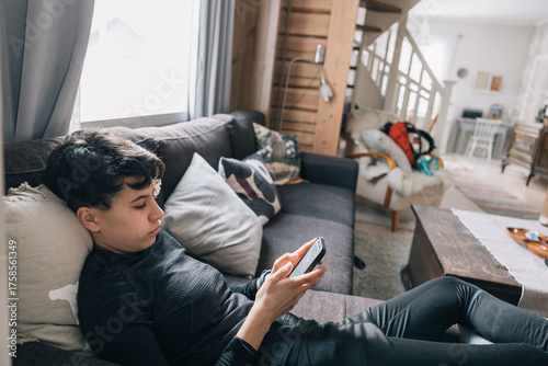 Teenager girl lying on a sofa and using a smartphone in a bright and cozy living room