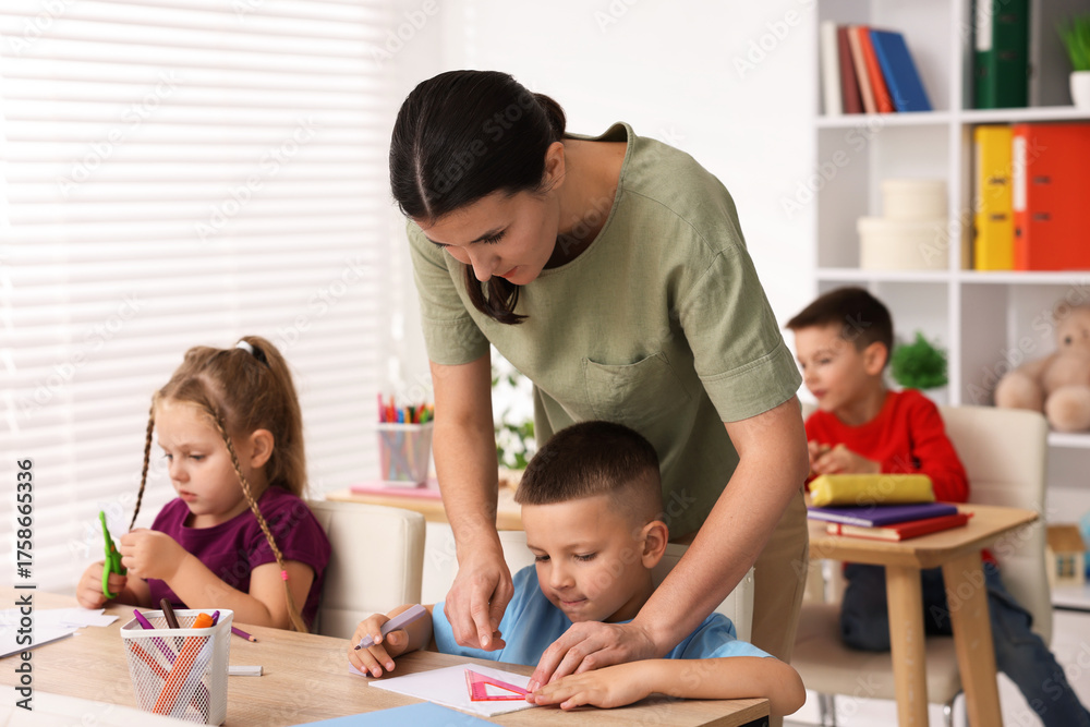 Fototapeta premium Children having lesson with teacher at wooden desk in elementary school
