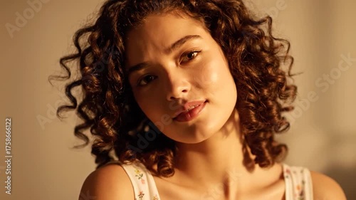 Portrait of a young woman with curly hair bathed in warm light.