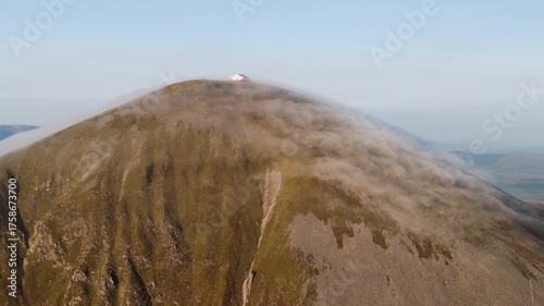 Amazing 4K aerial video of flying above and around Most Famous mountain in Ireland - Croagh Patrick in windy weather, with moving fog and clouds with breathtaking views around, Westport, Ireland