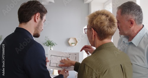 Back view of real estate agent holding project paper blueprint, discussing construction plan with senior family couple. Professional realtor explaining details, showing layout of apartment to clients.