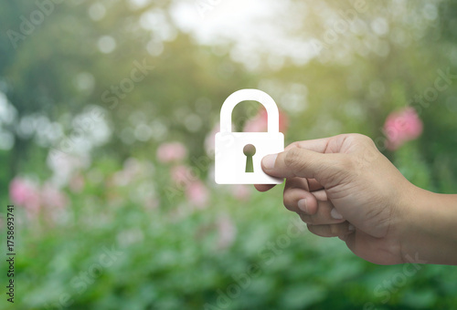 Hand holding padlock flat icon in fingers over blur pink flower and tree in park, Technology internet security and safety online concept
