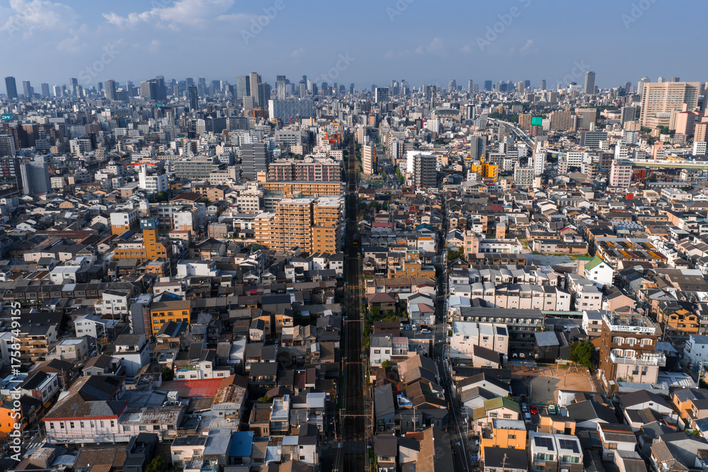 Fototapeta premium Aerial view of Osaka, Japan, with low and mid rise districts, a straight railway cutting center, and modern skyscrapers in soft daytime light under clear conditions.