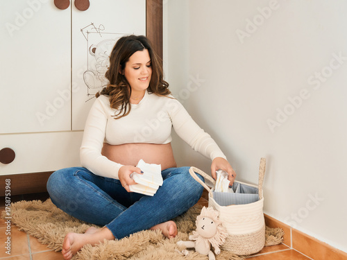 Pregnant woman organizing baby diapers in nursery room