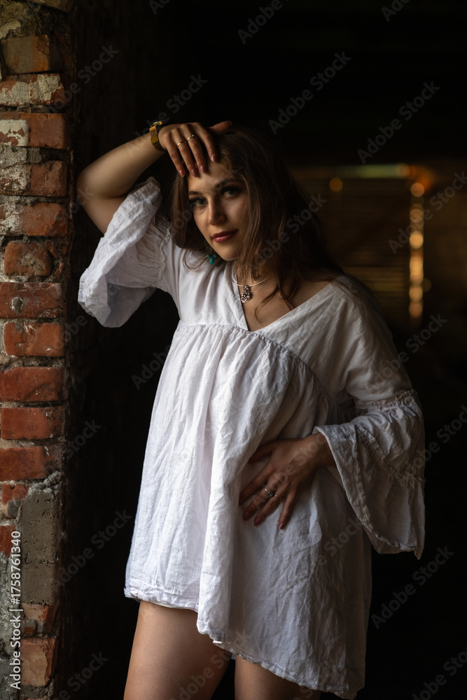 Obraz premium Young woman in a white dress stands playfully in an abandoned building, showcasing her joyful expression and the rustic surroundings, capturing a moment of carefree beauty