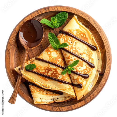 Thin pancakes on a wooden plate, drizzled with chocolate and garnished with mint