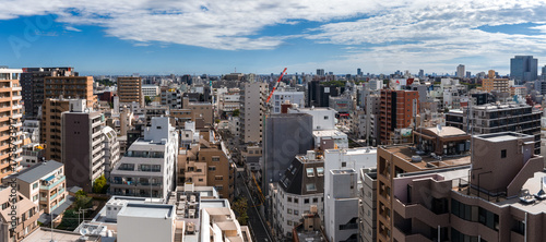 Photography Aerial view of Tokyo shows mid rise apartments, narrow streets, cranes, and distant towers under bright midday light with blue skies and scattered clouds