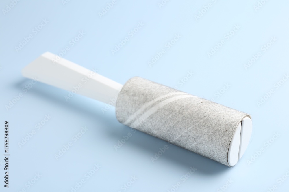 Obraz premium Lint roller with used sticky tape on light blue background, closeup
