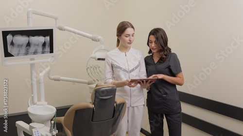 Two women dentist doctors are standing in a dental office and looking at a tablet