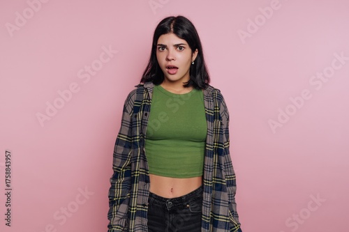 Young woman with dark hair expressing surprise against a pink background in casual clothing