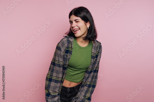 Young woman poses playfully in a casual outfit against a pink background during a personal photo session