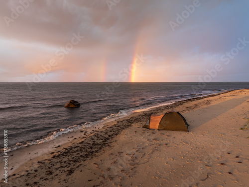 Fototapeta Naklejka Na Ścianę i Meble -  Camping tent on a wild sandy beach in Estonia with a stunning double rainbow over the Baltic Sea at sunset.