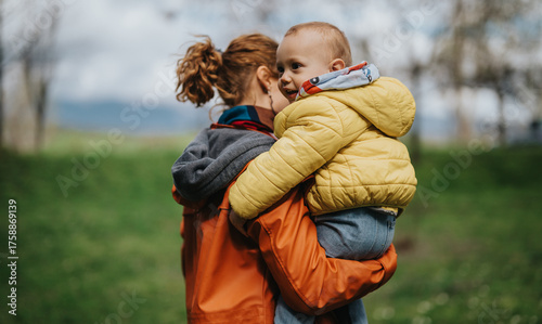Konstfotografi A mother is carrying her child on a spring day in a green outdoor area, showcasing family love, connection, and joy