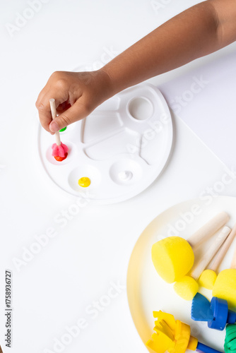 Child painting with colorful paints using wooden brushes on white palette