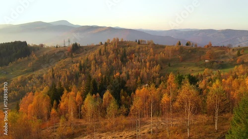 Warm sunlight illuminates mountain slopes with autumn forests in golden hues during sunset.