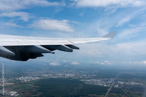 фотографія View from a window showing the aircraft wing flying over a mosaic of urban area, forests, and farmland