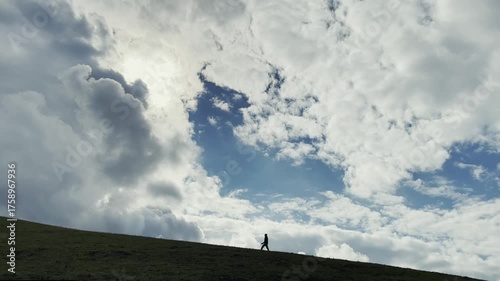 silhouette of a man walking on hillside under cloudy blue sky, xinjiang, china