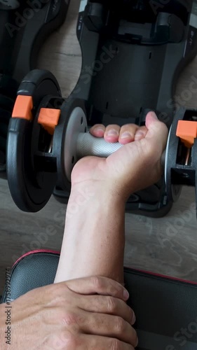 Athletic man lifting adjustable dumbbell at home.Vertical video