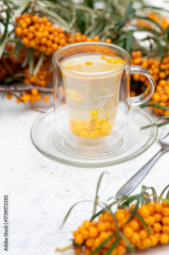 Sea buckthorn tea in a glass cup surrounded by fresh berries – healthy herbal drink