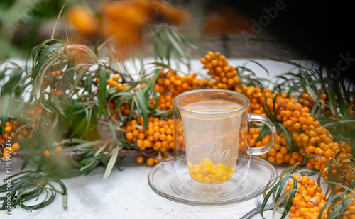 Sea buckthorn tea in a glass cup surrounded by fresh berries – healthy herbal drink