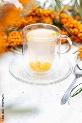 Sea buckthorn tea in a glass cup surrounded by fresh berries – healthy herbal drink