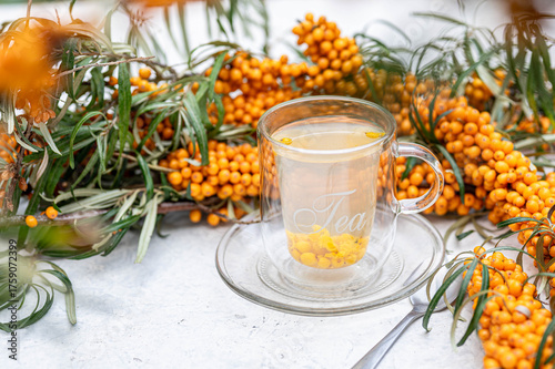 Sea buckthorn tea in a glass cup surrounded by fresh berries – healthy herbal drink