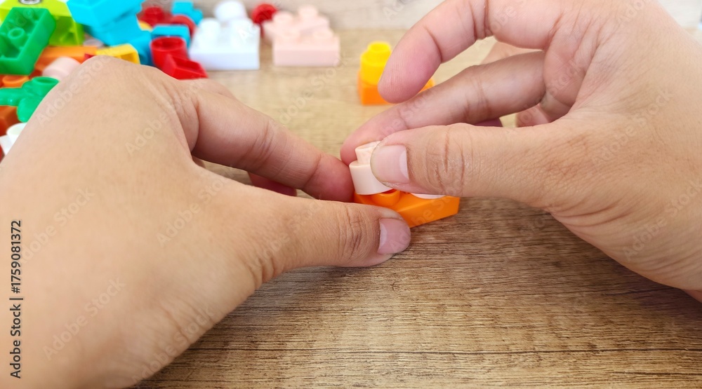 Fototapeta premium an asian woman is playing with lego forming the legs to form a giraffe with a brown background