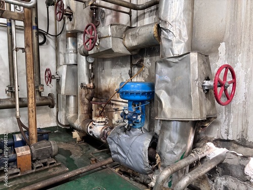 Complex network of industrial piping, pumps, and valves, showing the heavy-duty mechanical infrastructure of a boiler room, chemical, or power plant. The pipes and controls manage the flow of fluids i