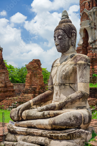 Old Buddha Statue Against Ancient Wat Mahathat in Ayutthaya Historical Park. Weathered stone Buddha statue seated amongst the majestic brick ruins at UNESCO World Heritage Site in Ayutthaya, Thailand