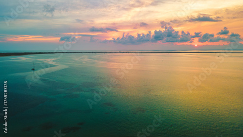 Obraz na plátně Aerial view of a sailboat gliding through turquoise shallows at sunset off the North Carolina coast, where golden light meets tranquil sea