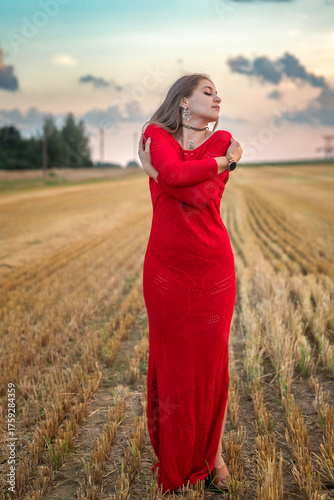 Obraz na plátně Young woman in a vibrant red dress stands gracefully in a golden field, with sof