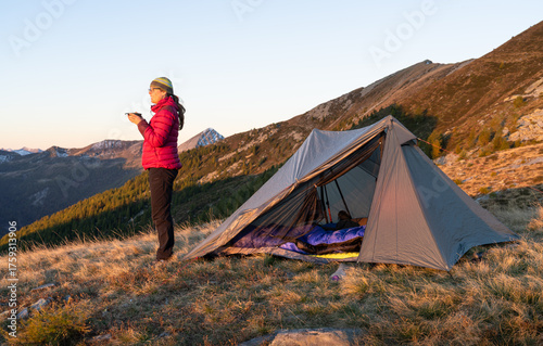 Woman in front of her ultra light tent enjoying the sunrise in the mountains.
