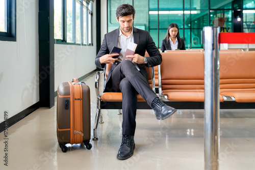 A businessman sitting on airport seat for waiting to check in at counter of airport to travel by aircraft.